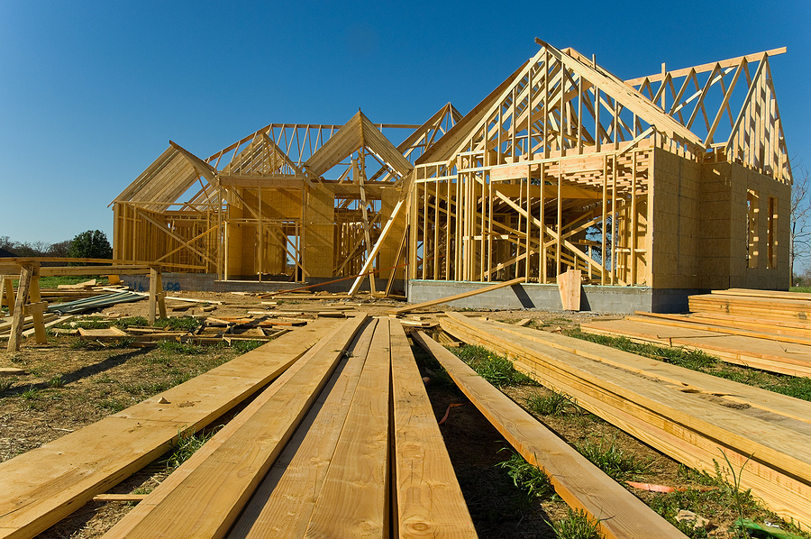 New home under construction with wood trusses and supplies against blue sky